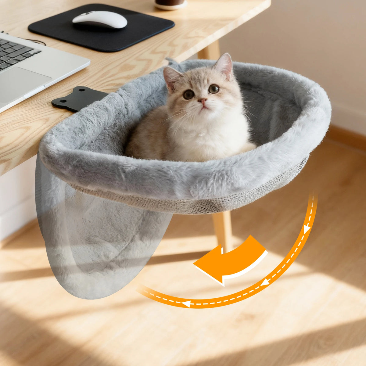 Lit de bureau pour chat en peluche grise fixé à un bureau en bois, chaton crème assis, flèche montrant le repli vers le bas