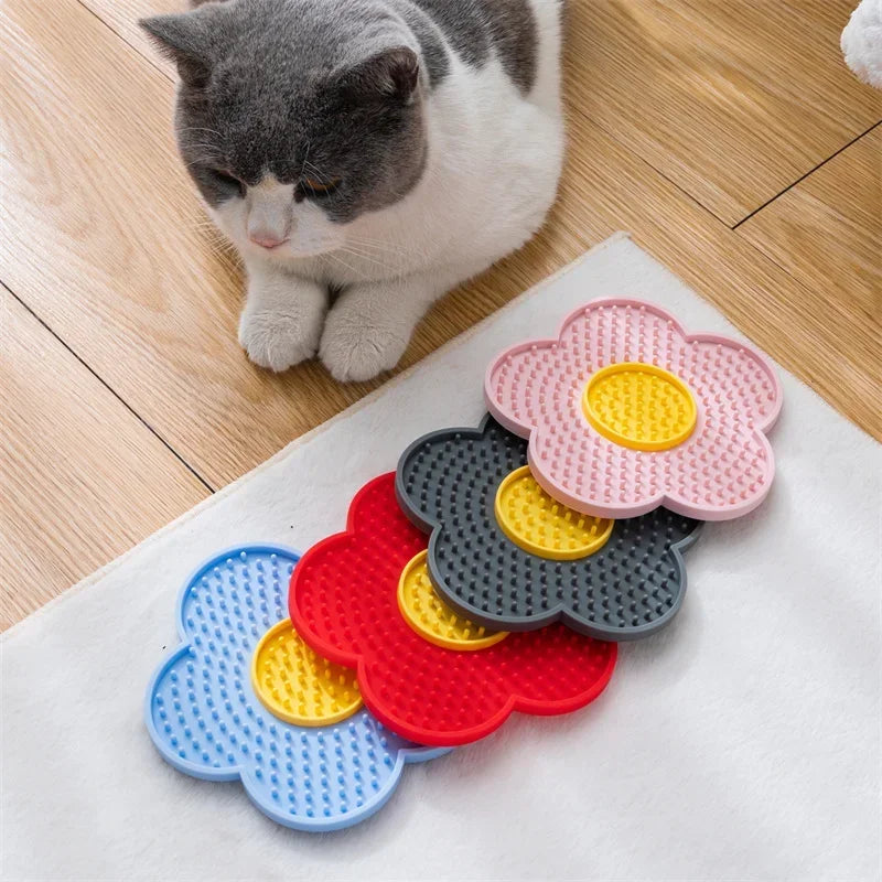 Chat couché près de quatre tapis de léchage en silicone en forme de fleur, en bleu, rouge, gris et rose