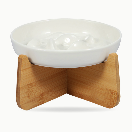 Gamelle anti-glouton pour chat en céramique blanche, poissons en relief au fond du bol, posée sur son support en bois en croix