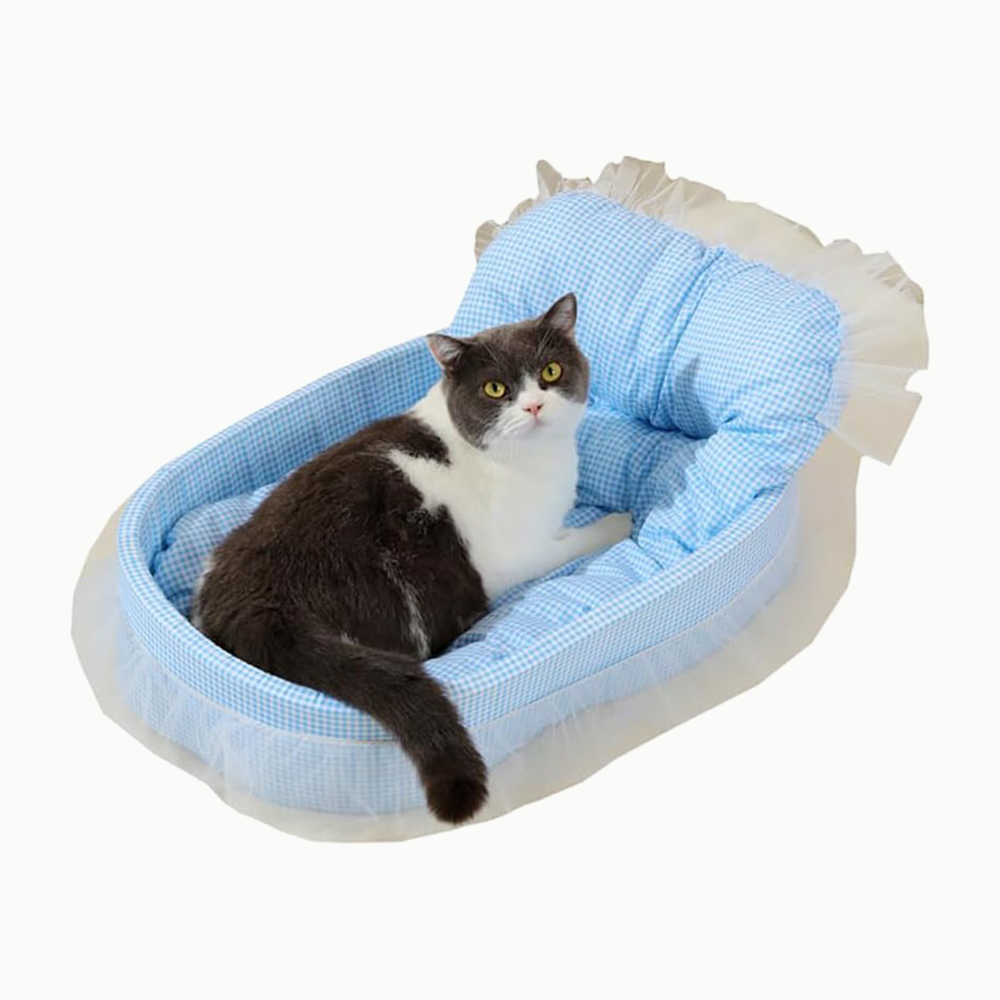 Panier pour chat ovale en vichy Le Boudoir Royal, bleu ciel, avec un chat gris et blanc couché dedans