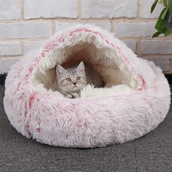 Chaton gris blotti dans le panier rose à capuche devant un mur de briques