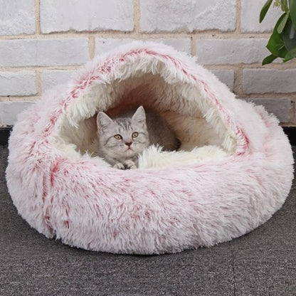Chaton gris blotti dans le panier rose à capuche devant un mur de briques