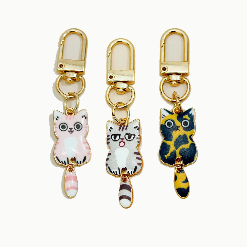 Trois porte-clés chat en métal émaillé, blanc et rose, gris tigré et bleu et or