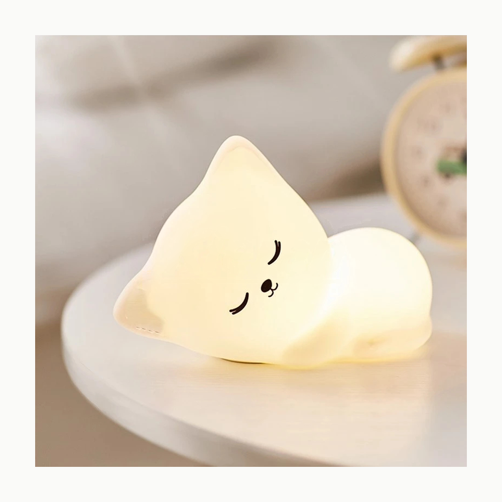 Veilleuse chat Le Veilleur Endormi, modèle tout blanc, allumée en lumière chaude sur une table de chevet